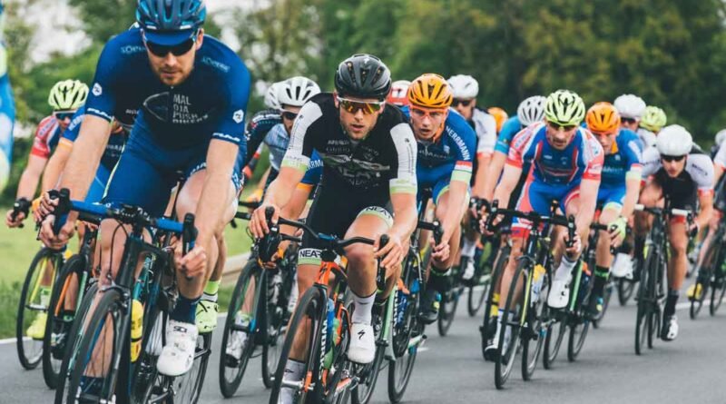 A pack of cyclists racing on a road, wearing colorful jerseys and helmets, leaning into a turn.