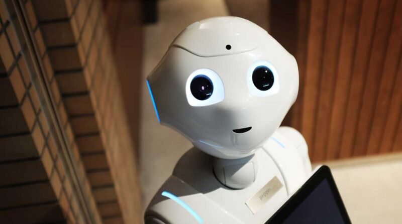White humanoid robot with large, expressive eyes and blue light accents, holding a tablet and wearing a name badge that reads 'Pepper' in a showroom or lobby setting.