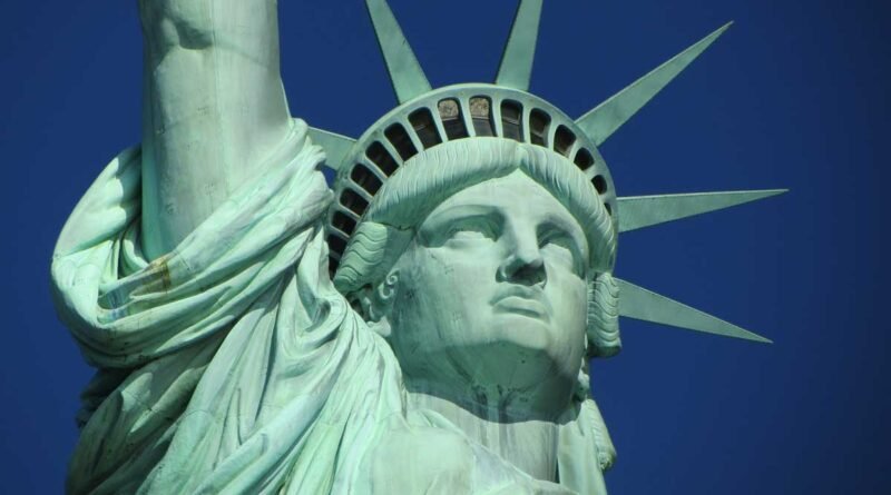 Close-up of the Statue of Liberty's face and crown with blue sky in the background, rays of the crown visible.